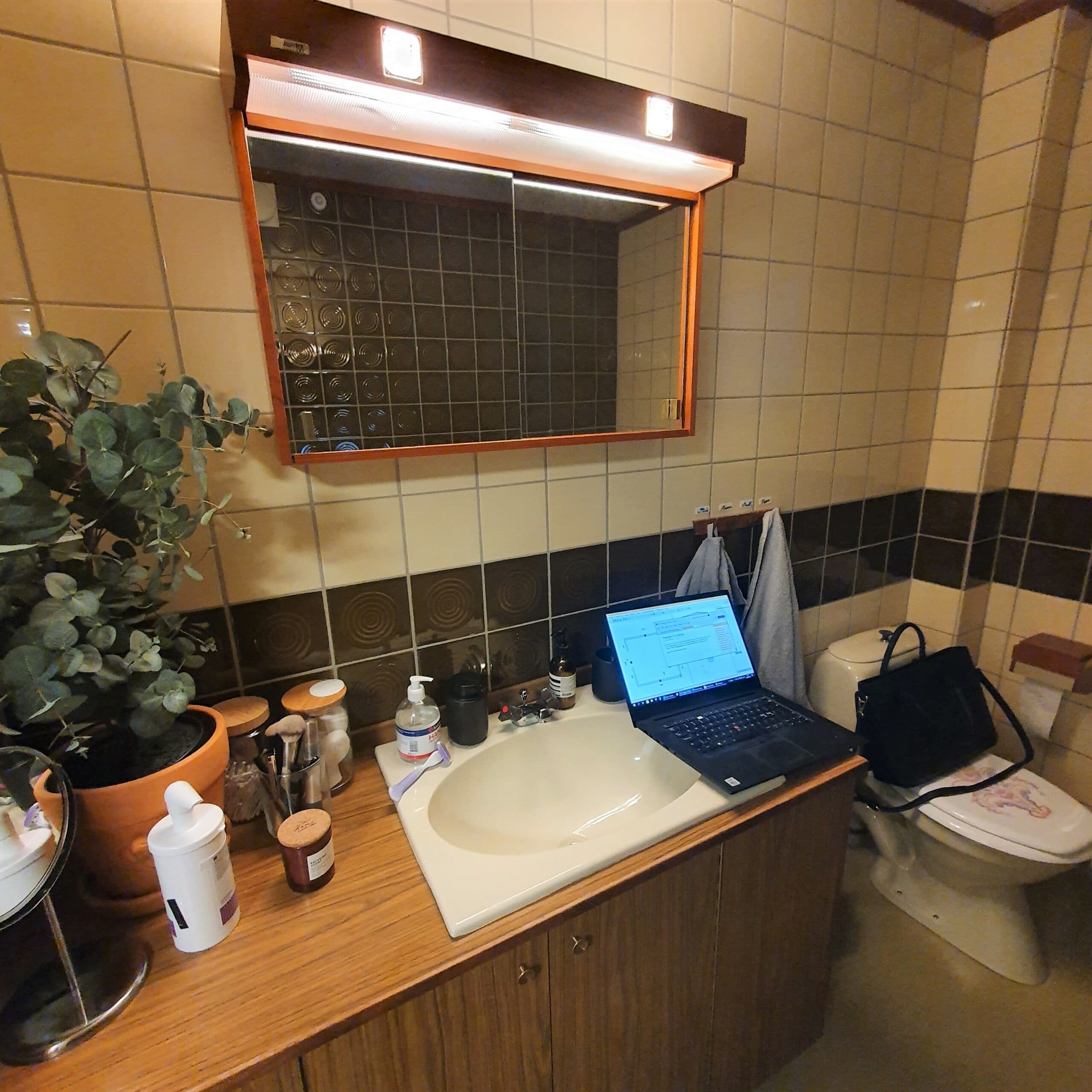laptop på träbänk i badrum. Upplyst spegel och en toalett