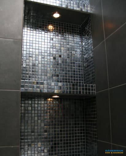 Badrum med belysta nischer i svart mosaik