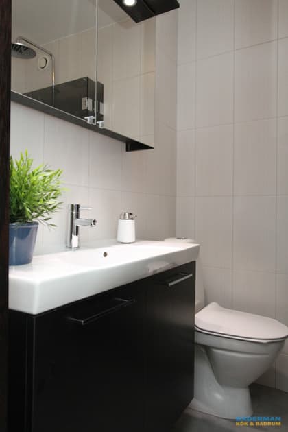 Badrum med vitt kakel och grå klinker