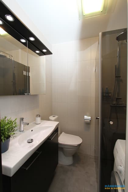 Badrum med vitt kakel och grå klinker