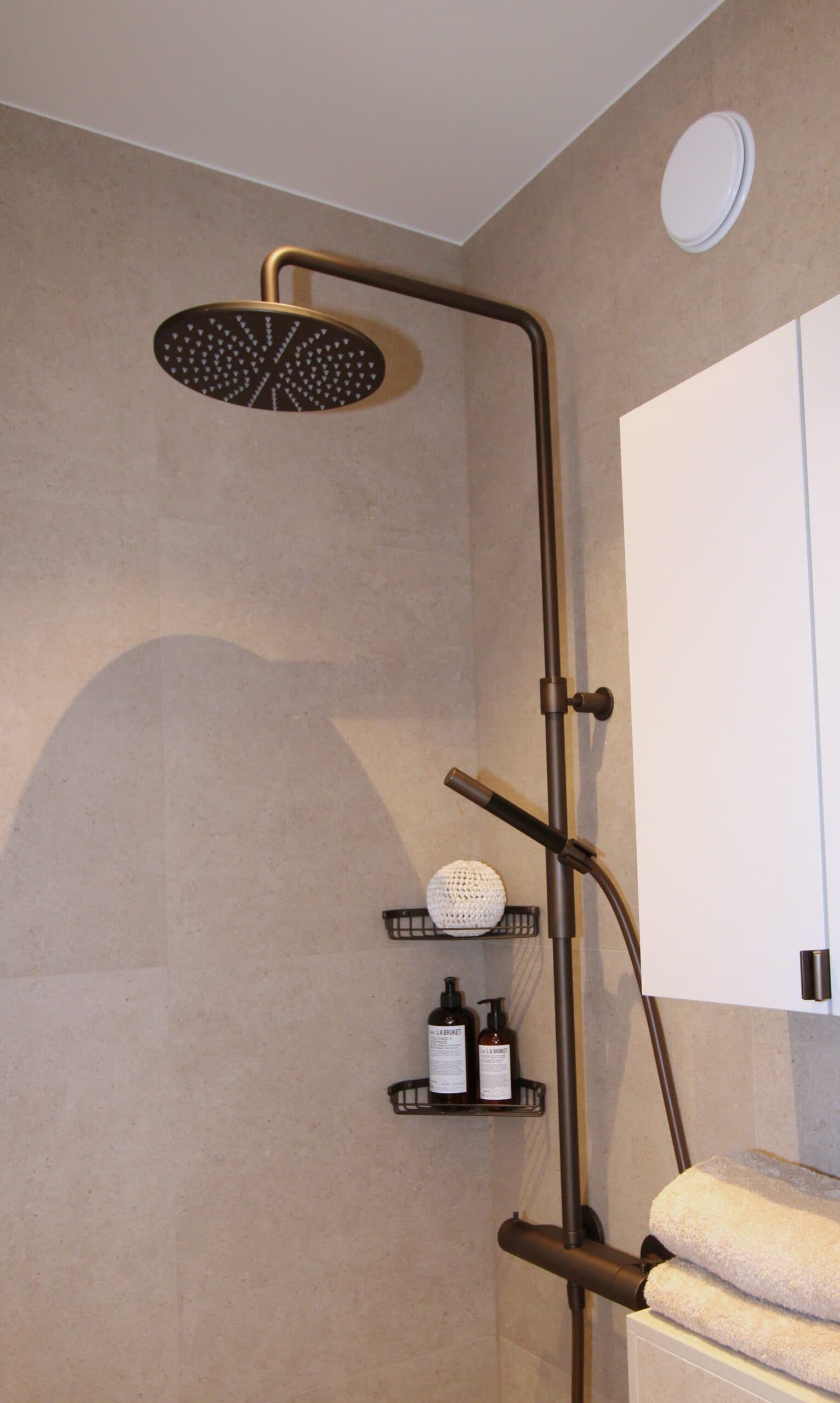 Svart vattenfallsdusch i nyrenoverat badrum med beige kakel och vita skåpsdörrar