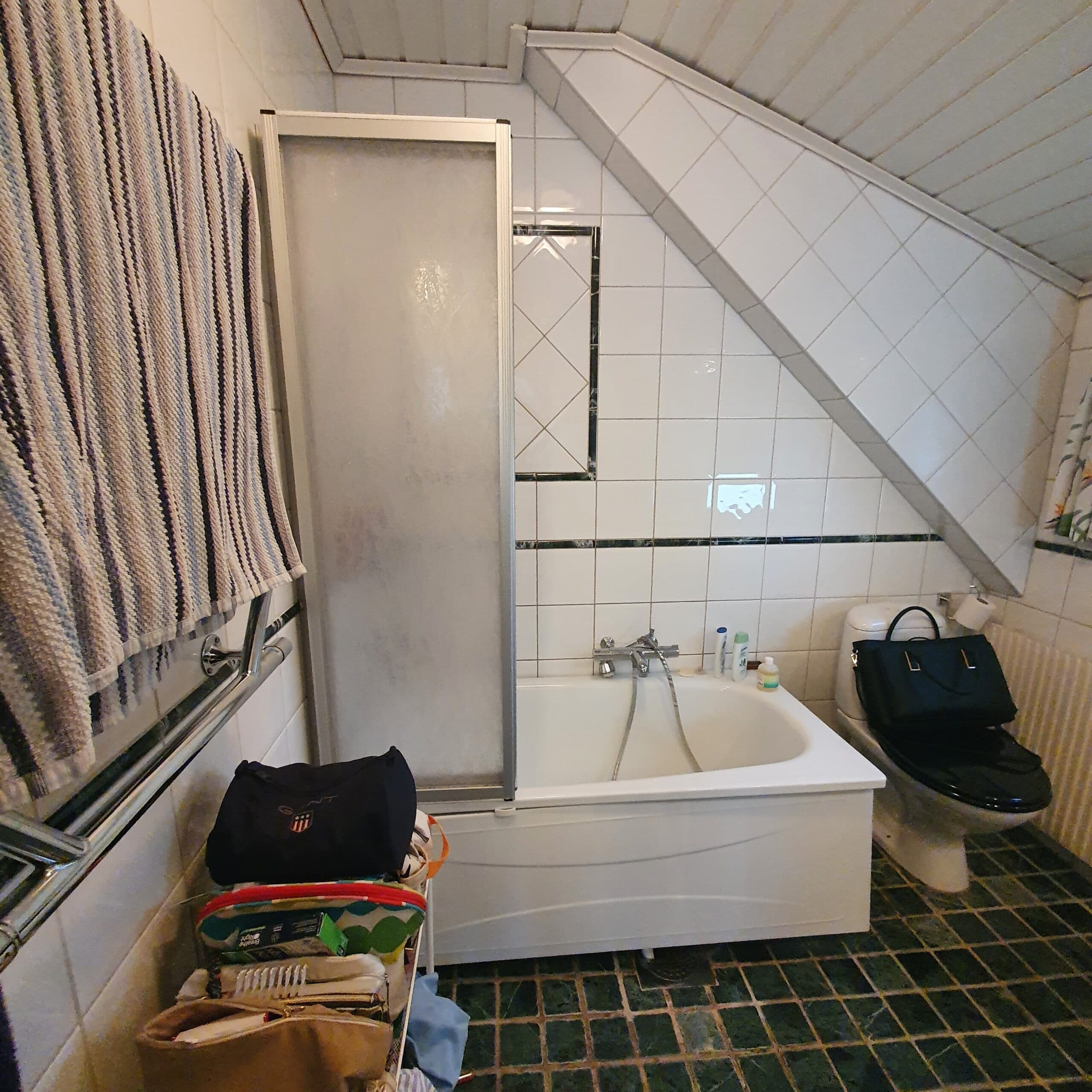 Badrum före renovering med äldre kakel, duschdraperi och traditionell inredning.