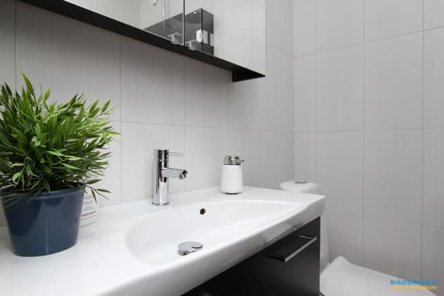 Badrum med vitt kakel och grå klinker